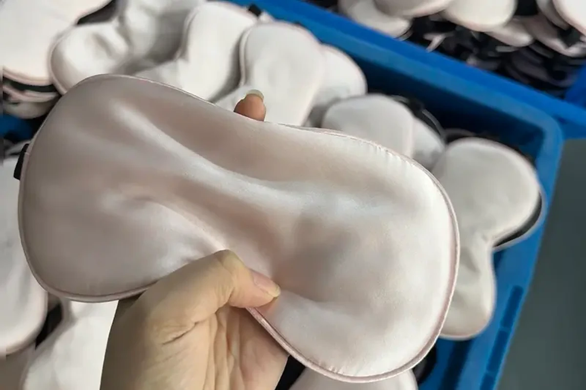Hand holding an ivory sleep mask beside a batch of finished masks