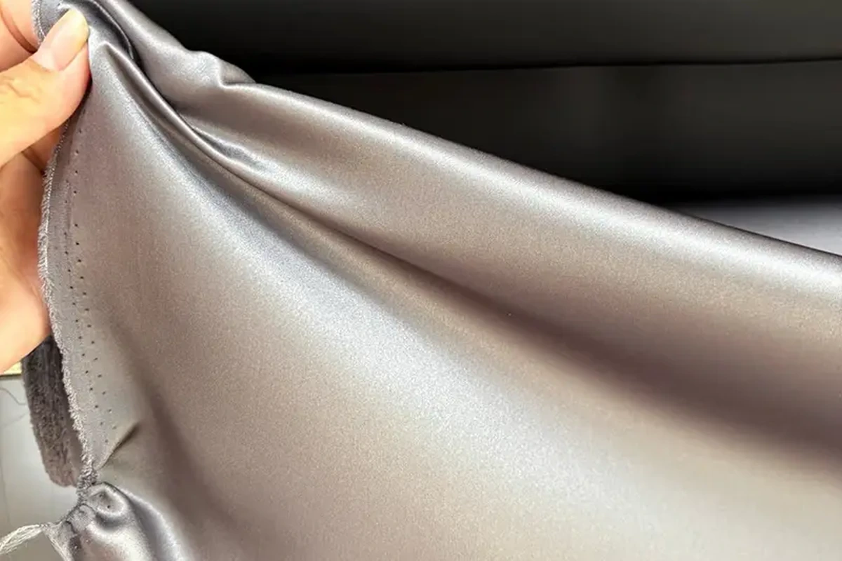 Hand lifting silver fabric to show its sheen and soft folds