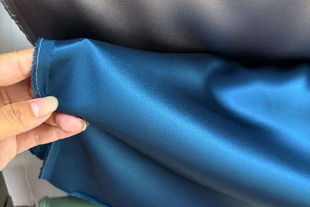 Hand holding blue fabric beside a darker roll to show the surface and folds