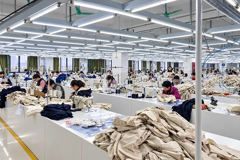 Garment workshop with rows of sewing stations and fabric panels on tables