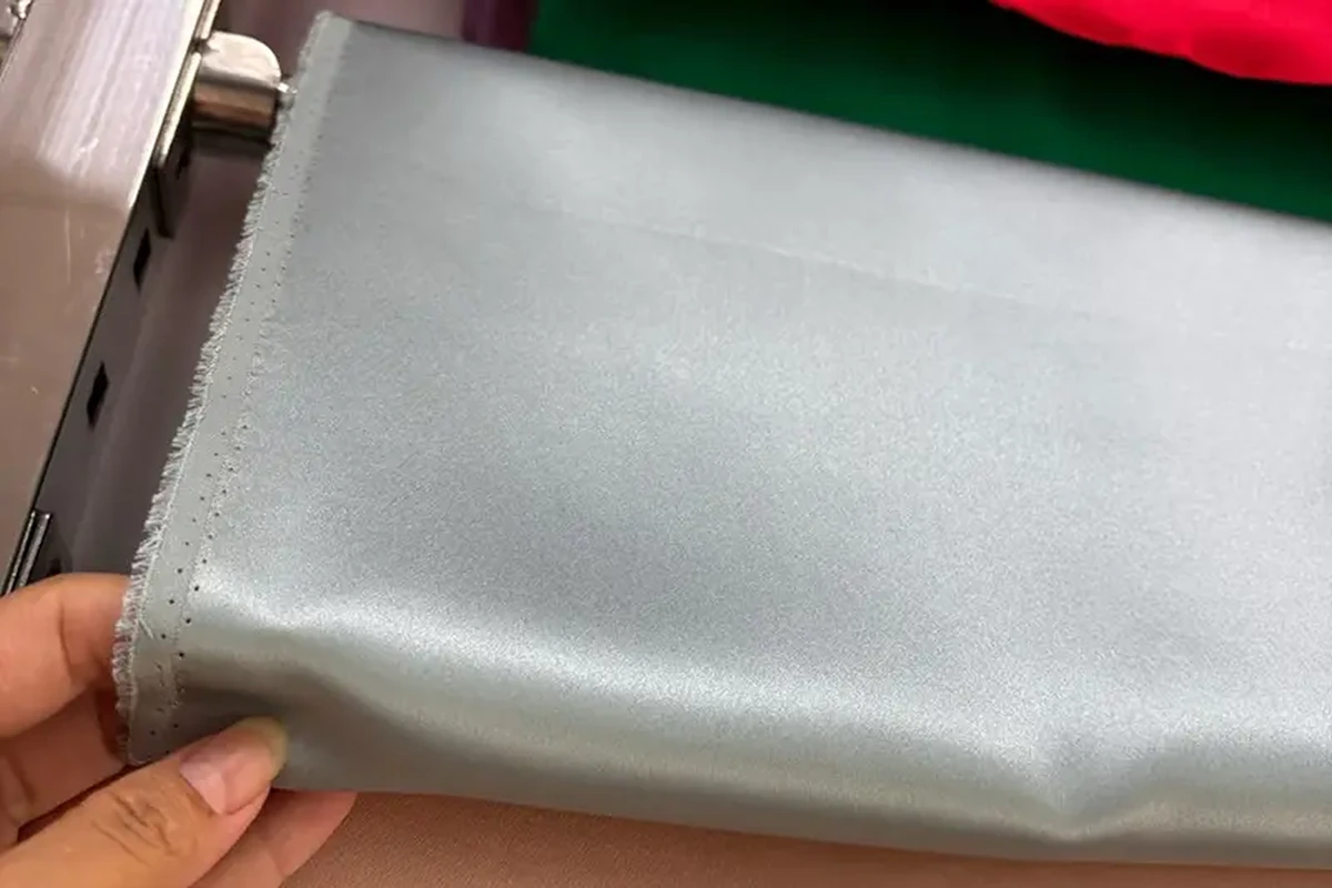Hand lifting a pale blue fabric sample from a display roll