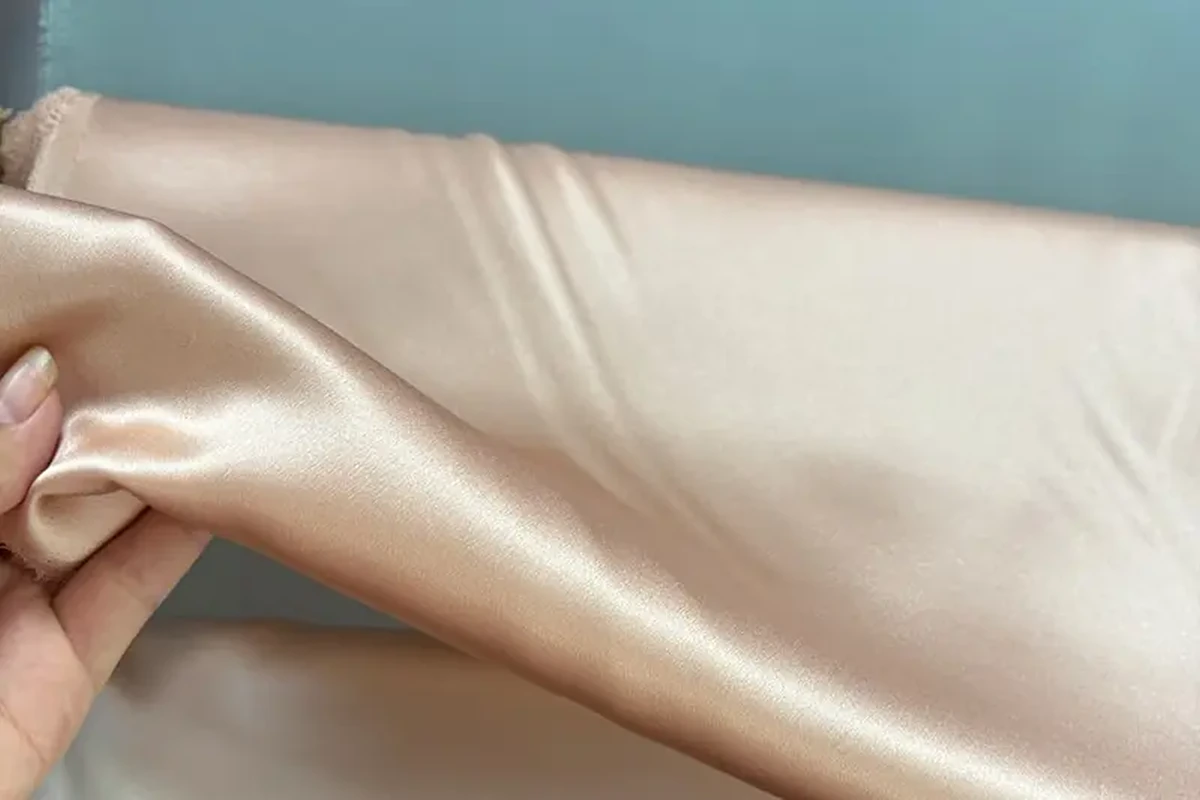 Champagne-colored fabric lifted by hand to show its sheen and drape
