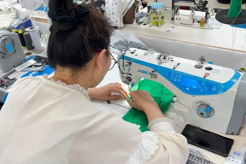 Worker guiding green fabric through an industrial sewing machine