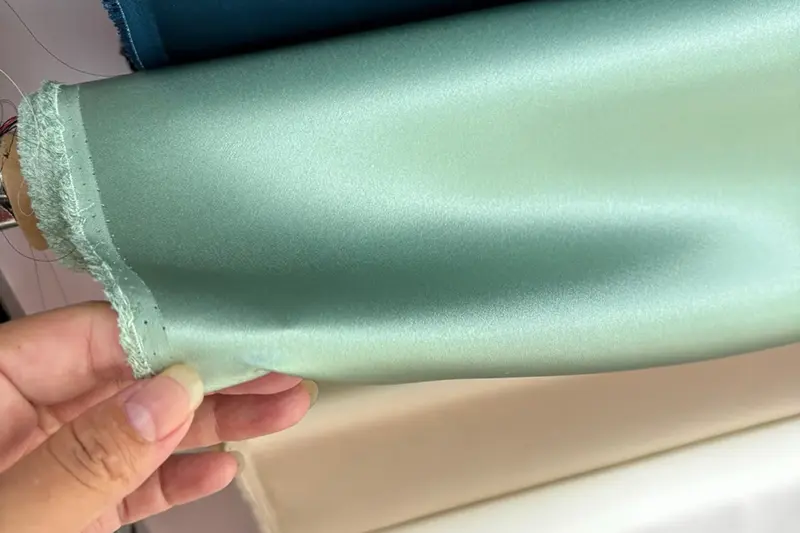 Mint green satin-weave fabric lifted from a roll to show its smooth surface