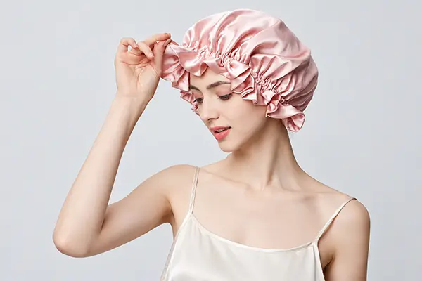 Model holding the gathered elastic edge of a pink silk bonnet