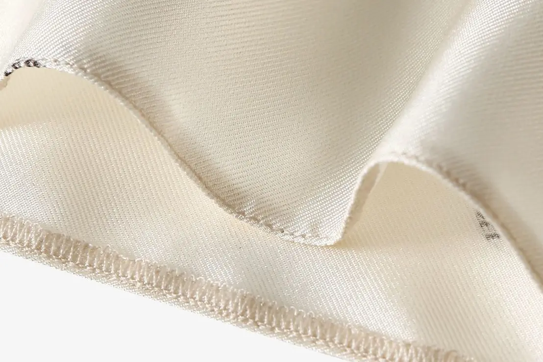 Close-up of stitching and a finished fabric edge on an ivory dress