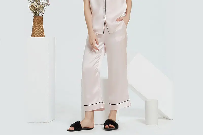 Pale silk pajama trousers with dark piping around the hems shown on a model