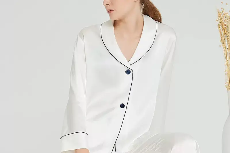 White silk pajama top with dark piping along the collar, button front and cuffs
