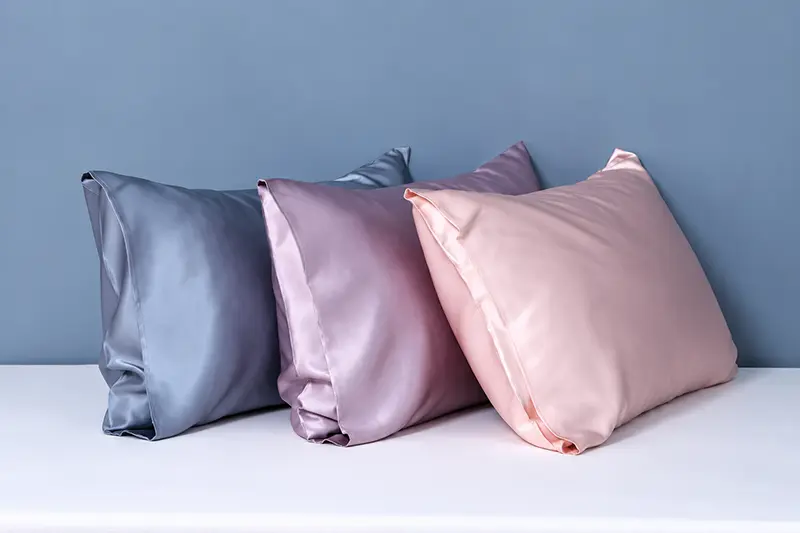 Three plain silk pillowcases in blue, mauve and pink arranged side by side