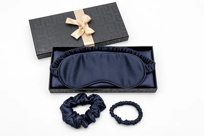 Navy sleep mask in an open ribbon-trimmed box with two scrunchies alongside