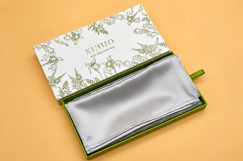 Silver silk pillowcase folded inside a floral-print presentation box