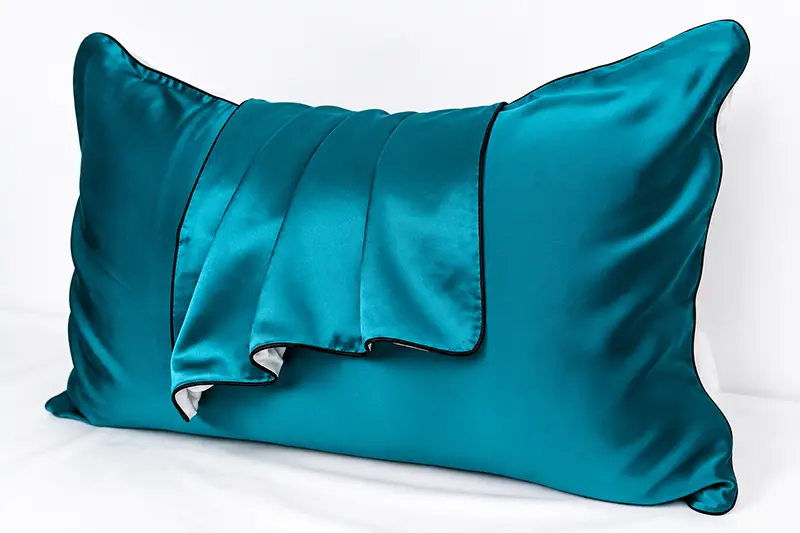 Teal silk pillowcase with dark piping and a folded corner revealing the edge