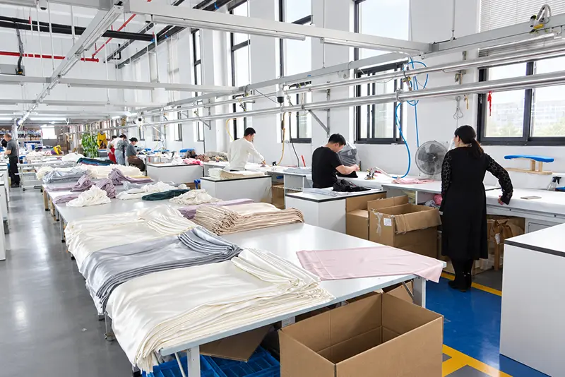 Workers pressing and folding textiles at long finishing tables