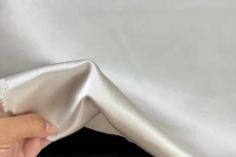 Hand lifting pale satin fabric to show the surface and curved folds