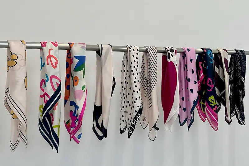 Scarves with varied prints and border colors hanging from a display rail