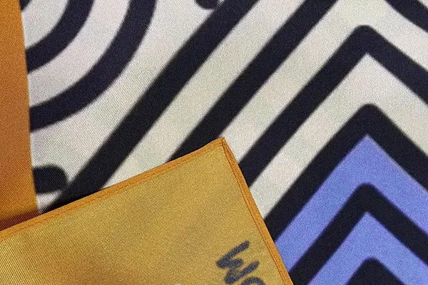 Close-up of a silk scarf's geometric print, diagonal texture and contrasting border