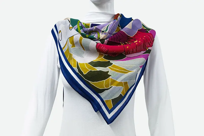 Multicolor printed silk scarf with a blue border draped around a mannequin
