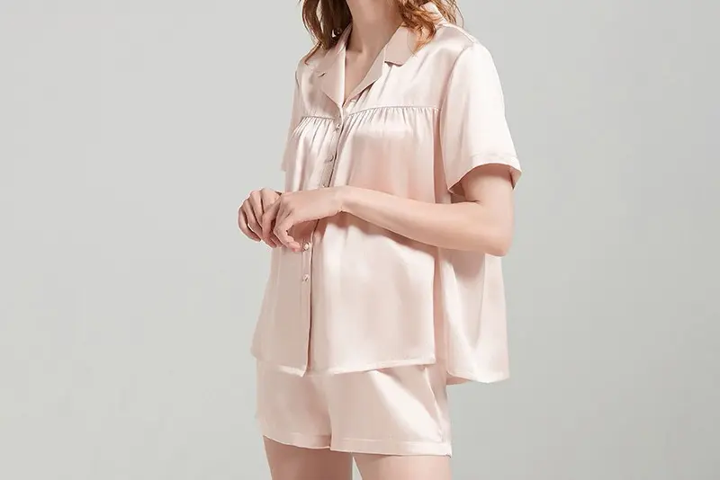 Pale pink short-sleeve silk pajama shirt and matching shorts shown on a model