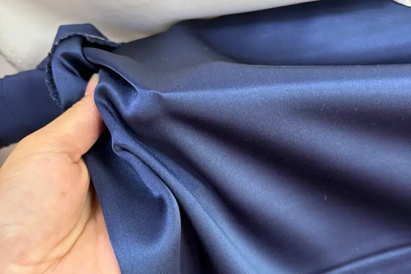 Hand gathering navy fabric to show its surface and folds